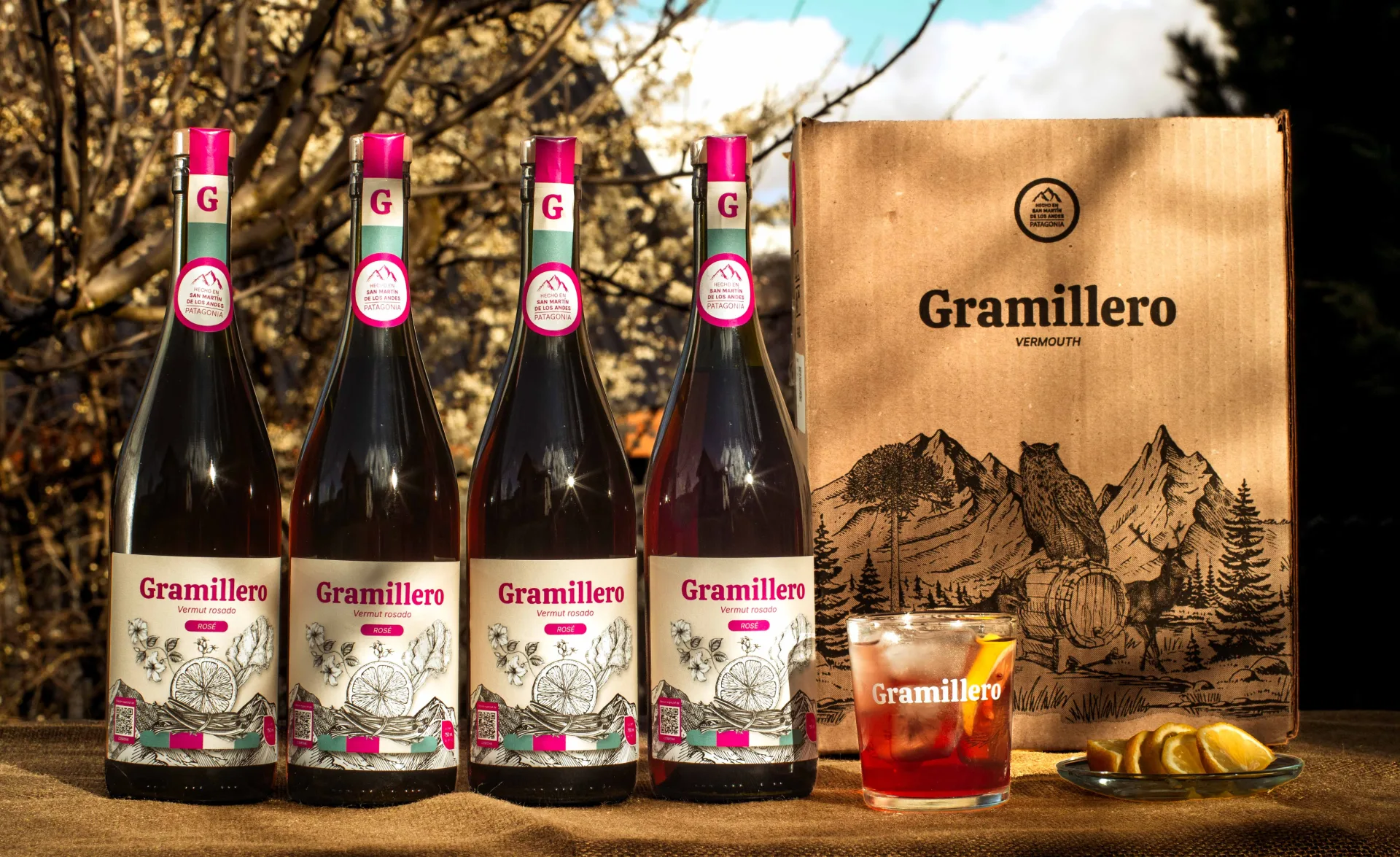 Cuatro botellas de Gramillero Rosado, caja Gramillero, vaso servido y rodajas de pomelo